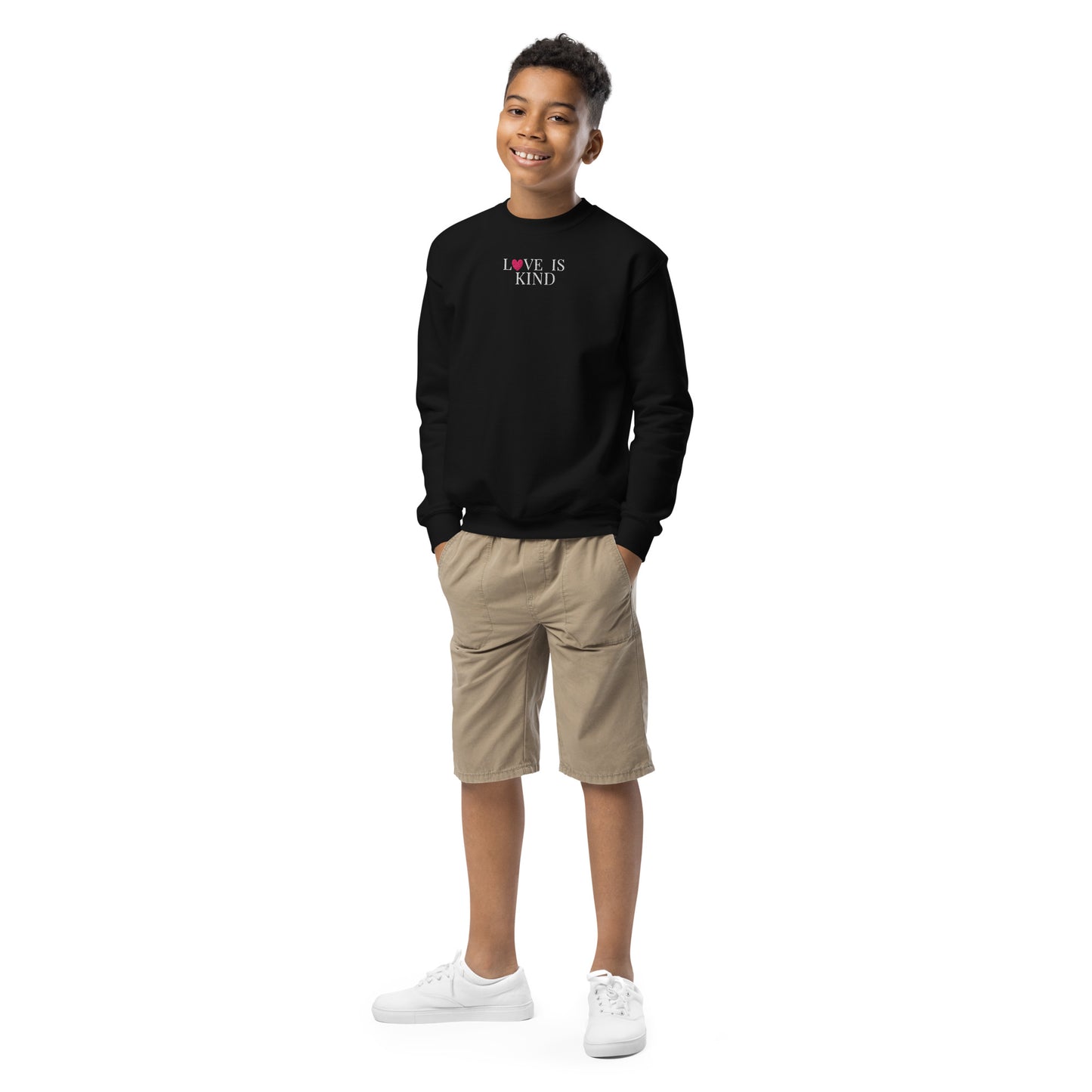 Child wearing a black sweatshirt with 'LOVE IS KIND' text, beige shorts, and white shoes on a white background