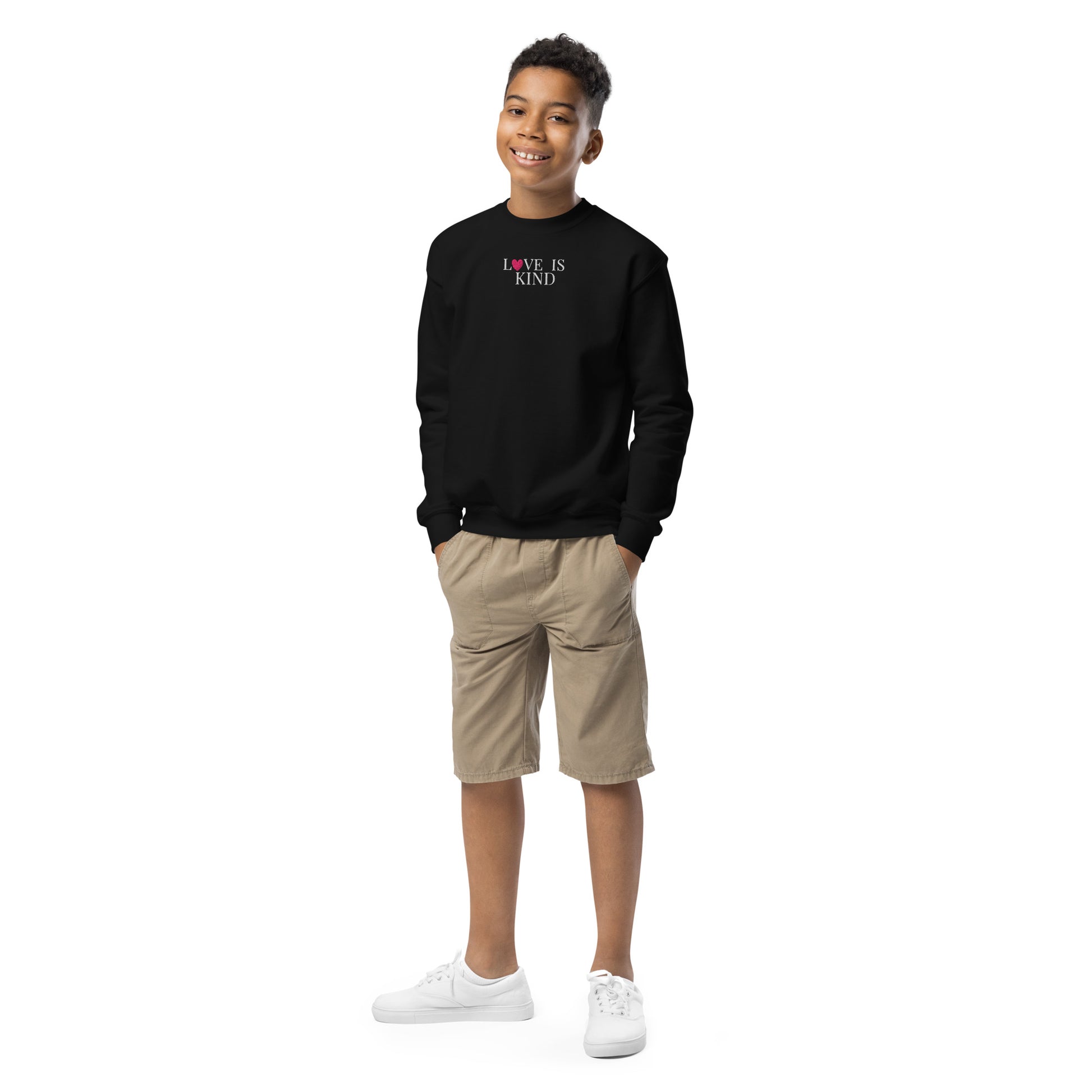 Child wearing a black sweatshirt with 'LOVE IS KIND' text, beige shorts, and white shoes on a white background