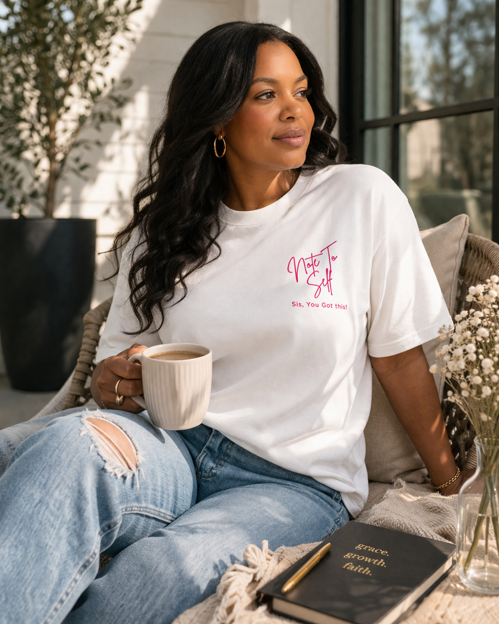 Black woman wearing white “Note to Self – Sis, You Got This” affirmation t-shirt, styled with light wash jeans and holding coffee in a cozy, sunlit home setting